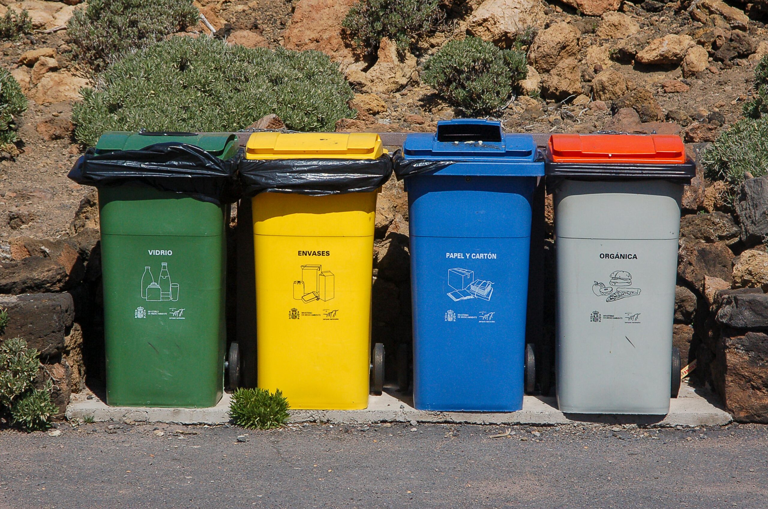 Four recycling bins for glass, packaging, paper, and organic waste outdoors.